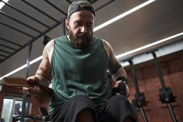 Scene of bearded man exercising in gym with determined facial expression. He is holding workout...