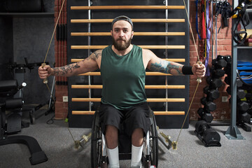 Man in wheelchair exercising with pulley system in fitness facility featuring various exercise equipment and machines around him