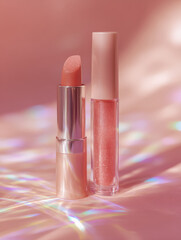 Beautiful side by side display of lipstick and lip gloss in soft rose tones, showcasing their glossy finishes against dreamy pink background. light reflects softly, creating magical atmosphere