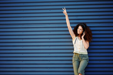 woman with headphones enjoying music while leaning against blue corrugated metal wall. curly hair...