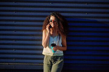 smiling woman with sunglasses talking on smartphone outdoors holding a coffee cup. casual style,...