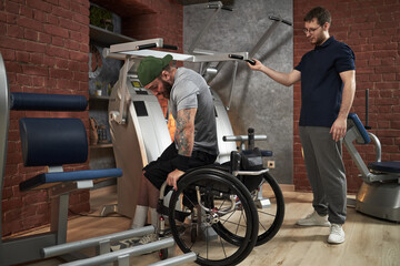 Encouraging individual in wheelchair participating in gym workout with assistance from trainer....