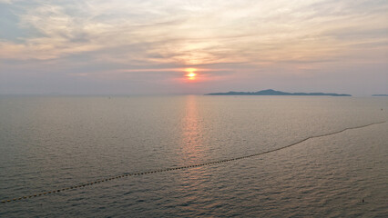 Golden hues of sunset paint the sky over a tranquil ocean, its surface reflecting the light as distant islands silhouette against the horizon, creating a serene and picturesque seascape