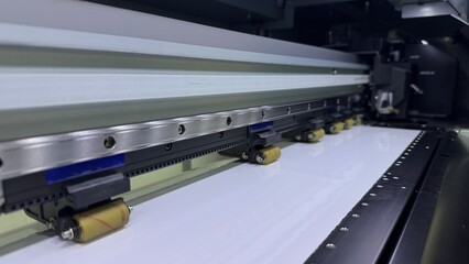 Large Format Printer in Action Close-up view of a large format printer during operation, showcasing the rollers and the movement of the printing material.  