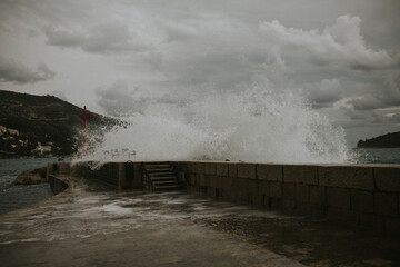 A powerful wave crashes against the historic port walls of Dubrovnik, sending a dramatic spray of water into the air