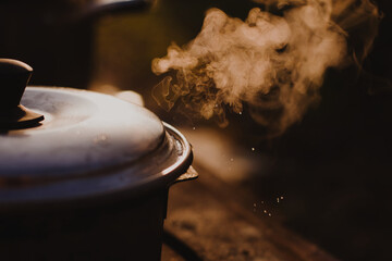 Steam rising from beneath a lid of a steel pot placed on a stove outdoors