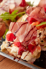 Detailed view of assorted bruschetta with ricotta, prosciutto, anchovies, tomato, arugula, and octopus on crusty bread slices.