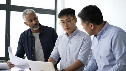 Three professionals review documents in a collaborative setting, likely files recently submitted. They stand around a laptop, deeply engaged with the task.

