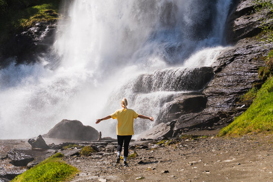 A girl admires the majestic Steinsdalsfossen waterfall in Norway, walking behind the wall of water on a summer day among rocks and greenery.