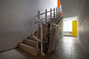 A modern staircase in a building interior features a stairlift for people with limited mobility, also known as reduced mobility, experience difficulty in moving around independently