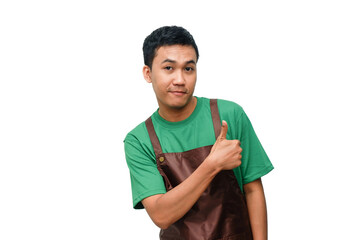 Smiling young man in green shirt and brown apron giving a thumbs-up with a friendly and...
