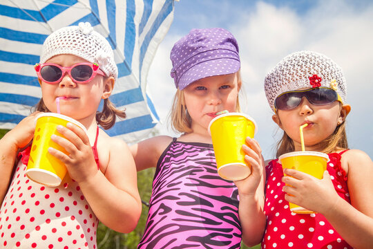 Little girls in bathing suits drinking sweet drinks from a straw under a sun umbrella