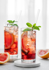 Two glasses of cocktail with grapefruit, mint and ice on a table against a window with natural light