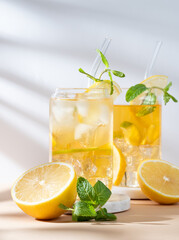 Two glasses of iced tea with lemon, mint and ice on a marble stand on light background