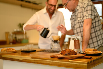 Sliced loaf of bread on a wooden countertop with father and son preparing coffee in background