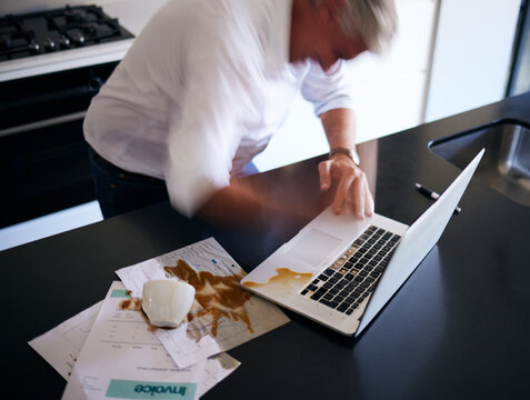 Laptop, documents and man spill coffee, mistake or accident in home kitchen. Angry, spilling tea on computer and paper of mature male person, freelancer or remote worker with error, problem or clumsy