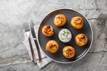 Baked Knysh pies with onion potato filling served with sour cream close-up in a plate on the table. Horizontal top view from above