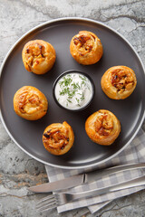 Classic potato knish with jammy onions and flaky crust served with sour cream closeup on the plate on the table. Vertical top view from above