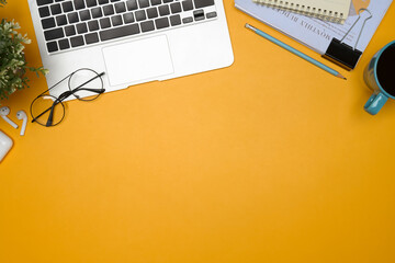 Creative desk with laptop, coffee cup, and accessories on vibrant yellow background.