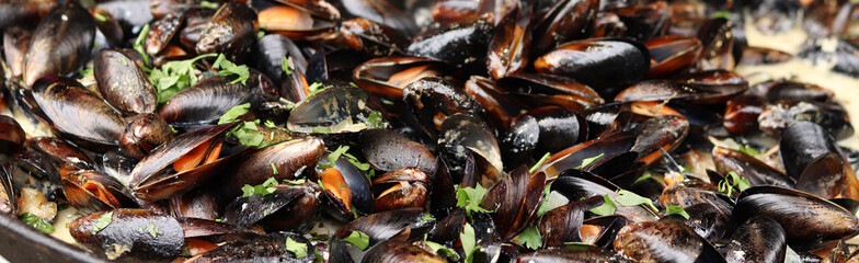 Mussels with parsley and sauce in a large frying pan. Food court. Street food. Mussels with shells cooked with herbs in a frying pan. Mussels cooked in sauce at a street market. Cooking a seafood dish