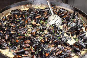 Mussels with parsley and sauce in a large frying pan. Food court. Street food. Mussels with shells cooked with herbs in a frying pan. Mussels cooked in sauce at a street market. Cooking a seafood dish