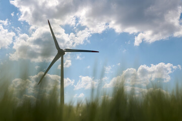 Single wind turbine silhouetted against bright blue sky with scattered fluffy clouds and blurred...