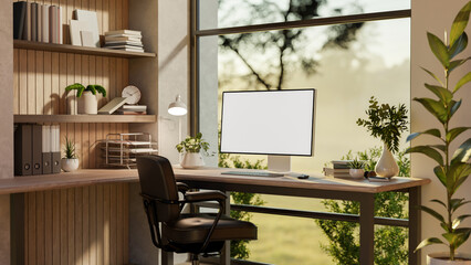Blank screen computer on a wooden table and armchair near glass wall with nature view outside.
