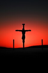 Fototapeta premium A silhouette of a man holding a cross is standing in front of a fence
