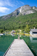 A sunny view of the quiet wooden pier in Loen, Norway, with the Loen Skylift ascending to Mount Hoven in the background, surrounded by majestic fjord landscapes