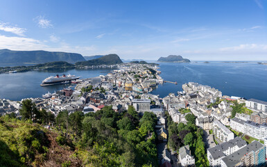 Panoramic view of Alesund in Norway from Aksla mountain, with colorful Art Nouveau buildings, cruise ships docked in the harbor, and surrounding fjords and islands in a sunny day