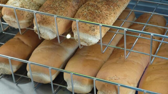 Various types of bread, including baguettes and sub rolls, cool on metal racks