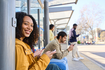 Young woman smiling and using mobile phone at bus stop