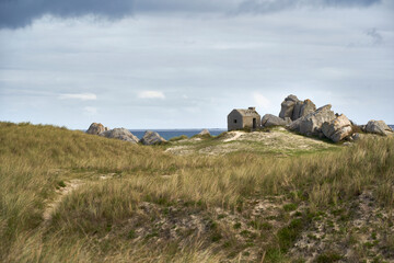 A small stone watch post stands on a grassy hill under a dramatic sky, showcasing the rugged beauty of Brittany. Plage des Amiets, France.