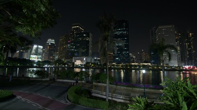 This video showcases the vibrant nighttime scenery of Bangkoks skyline with illuminated skyscrapers along the citys bustling riverfront, reflecting Thailands urban beauty.