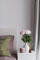 Simple Bedroom Styling with Pastel Pink Peonies in a Ceramic Vase, Scented Candle, Reed Diffuser. Minimal Interior Decor