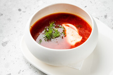 A bowl of Ukrainian borscht with sour cream and fresh dill, served on a white plate. The vibrant red color contrasts with the creamy garnish, highlighting the traditional homemade dish.