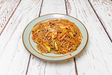 Blue porcelain plate with a stew of thin transparent noodles stir-fried with vegetables