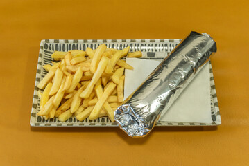 A durum wheat bag wrapped in aluminum foil with chips and a napkin on a yellow table.