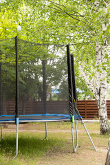 Trampoline with safety net in the park among trees in summer, active outdoor recreation