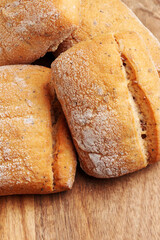 Fresh wheat bread buns with golden cracked crust on wooden table. Macro shot. 