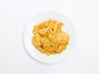 Top view of a white plate filled with crispy golden tempeh chips, a traditional Indonesian snack, isolated on a white background.
