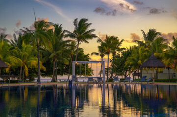 Sunset view of a luxury resort pool with palm trees, lounge chairs, and beach access in Mauritius.