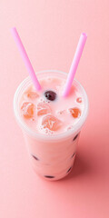 Iced pink bubble tea with tapioca pearls, served in a clear plastic cup with two pink straws on a pastel pink background