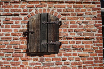 Brick wall featuring a window with a wooden shutter secured by rustic metal hinges, Nidzica, Poland