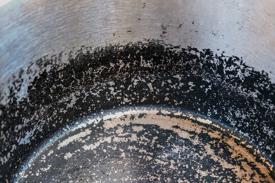 Stainless steel pot with a heavily burnt and blackened interior surface, showcasing the effects of high heat and residue accumulation