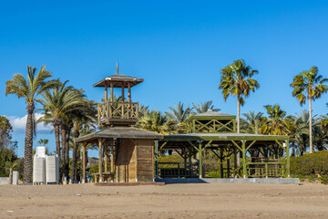 Wooden beach structure with lifeguard tower, terrace and sun loungers on sandy shore under palm trees. Antalya, Turkey, Mediterranean.