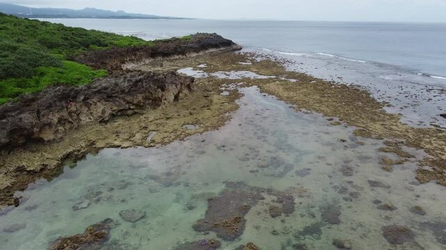 4K The serene seascape of Okinawa showcases crystal-clear waters, exposed rocky formations, and gentle waves lapping against the shore