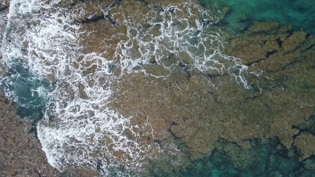 4K The serene seascape of Okinawa showcases crystal-clear waters, exposed rocky formations, and gentle waves lapping against the shore
