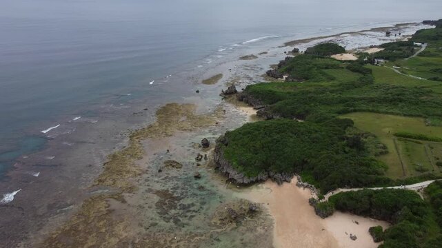 4K The serene seascape of Okinawa showcases crystal-clear waters, exposed rocky formations, and gentle waves lapping against the shore