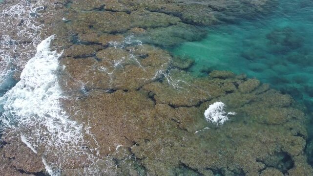 4K The serene seascape of Okinawa showcases crystal-clear waters, exposed rocky formations, and gentle waves lapping against the shore